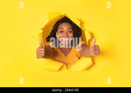 Schwarze Dame Gestikuliert Die Daumen Durch Zerrissenes Papier, Gelber Hintergrund Stockfoto