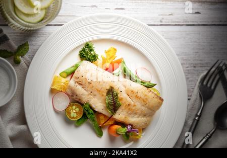 Ein Blick von oben auf einen gegrillten Fisch mit Gemüse auf einem weißen Teller Stockfoto