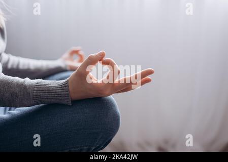 Nahaufnahme einer nicht erkennbaren friedlichen jungen Frau, die in Lotuspose und Meditation sitzt, Yoga zu Hause praktiziert, Hände Finger, ruhiges Mädchen, das sie kontrolliert Stockfoto