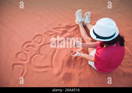 Schöne junge Frau, die mit Sand auf einer Sanddüne aus der Wadi Rum Desert spielt, auch Wally des Mondes genannt, aus Jordanien. Urlaub nach Jordanien. Stockfoto