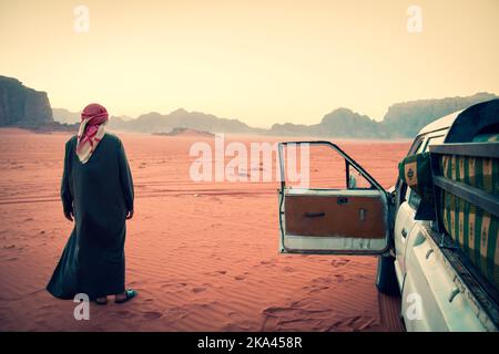 Beduinen-Fahrer-Tour-Organisator steht in der Wadi-Rum-Wüste mit einem Allradfahrzeug nach Sonnenuntergang. Besuchen Sie Jordanien Touren im berühmten Wadi Rum Reserve Mitte Stockfoto