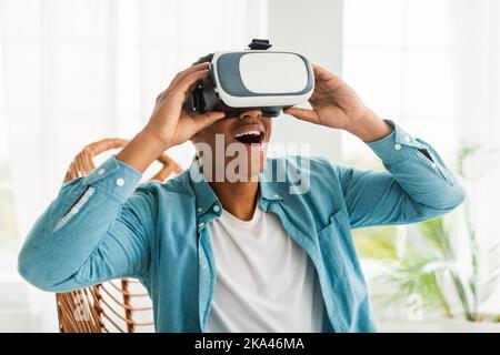 Glücklich inspirierten jungen schwarzen Mann in VR-Brille mit offenem Mund genießen Online-Virtual-Reality-Spiel Stockfoto