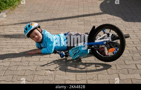 Ein Kind mit Schutzhelm fiel im Park von einem Fahrrad ab Stockfoto