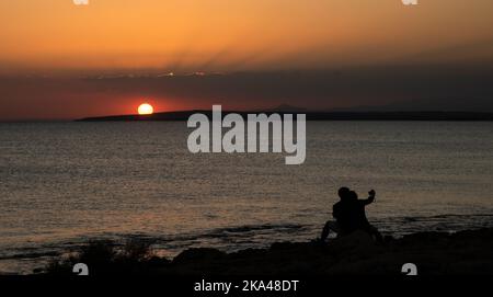 Silhouette eines jungen Paares, das den wunderschönen Sonnenuntergang am Strand genießt. Romantische Moment menschliche Beziehung Stockfoto