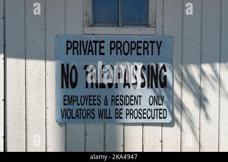 Ein weißes Schild mit schwarzen Buchstaben auf einer weißen Wand, auf der steht: „Private Property“, „No Trespassing“. Stockfoto