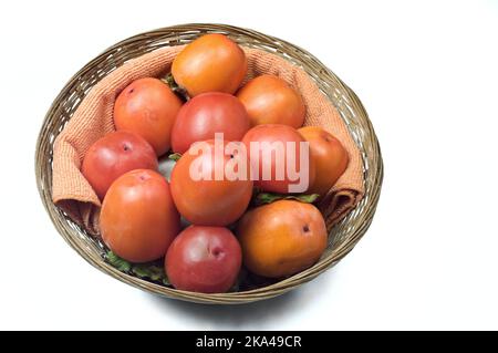 Bio-Kaki aus dem Herbstgarten in einem Weidenkorb auf weißem Grund. Stockfoto