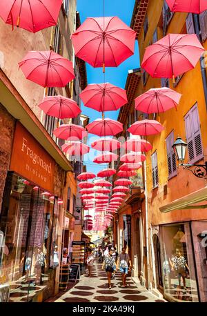 Grasse, Frankreich - 6. August 2022: Historische Mietshäuser und enge Straßen mit rosa Regenschirmen aus dem alten Stadtviertel der Parfümerie-Stadt Stockfoto