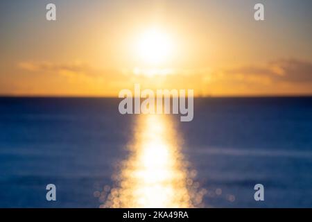 Unscharfer Hintergrund. Sonne scheint in den Himmel während Sonnenuntergang Dämmerung. Sonnenaufgang dämmert Sonnenuntergang. Sonniger Pfad, sonniger Gehweg auf der Oberfläche von Meereswellen. Sonnenstrahlen. Meereslandschaft. Natürliche, unscharfe Bokeh-Textur Stockfoto