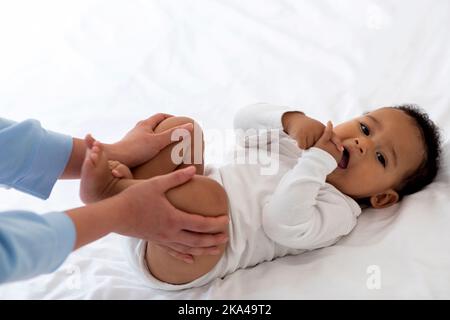 Verstopfung Bei Babys. Fürsorgliche Mutter Macht Gymnastik Mit Schwarzem Kleinkind, Nahaufnahme Stockfoto