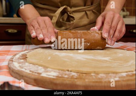 Details: Koch Konditoren Hände mit Nudelholz, Rollen Sie den Teig auf einem bemehlten Holzbrett. Backkonzept. Stockfoto