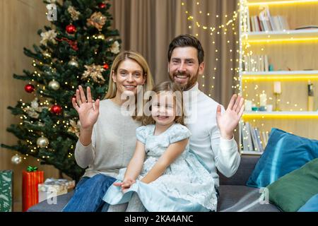 Familie Eltern und kleines Mädchen Kind Gruß Remote Videokonferenz Chat Anruf online Gespräch Glückwünsche Frohe Weihnachten Frohe Weihnachten Frohe Weihnachten Winterferien Blicke auf Kamera Webcam Ansicht. Stockfoto