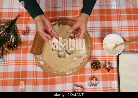 Weihnachtliche Küche mit den Händen des Küchenchefs, die mit Ausstechformen aus dem Lebkuchenteig Formen schnitzen Stockfoto