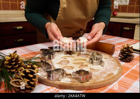 Beschnittene Ansicht einer Hausfrau in beigefarbener Kochschürze, die der Kamera Weihnachtskekse zeigt, die aus Lebkuchenteig herausgeschnitten wurden Stockfoto