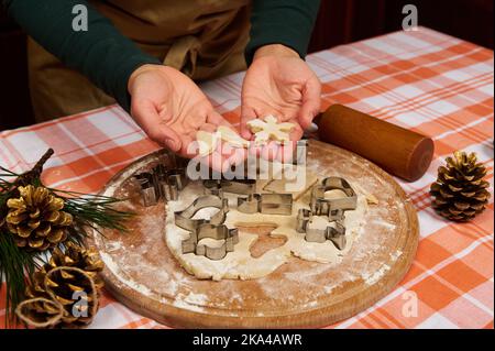 Geschnitzte Schneeflocke und Engelsflügel aus Teig in den Händen des Konditors, die Lebkuchen für Weihnachten zubereiten. Stockfoto