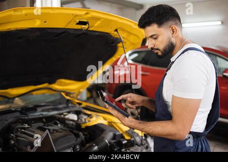 Serious fokussierten Mann Auto Techniker Mechaniker Reparatur Auto Problem des Motors, während der Systemprüfung Detail, mit Tablet-Computer für die Wartung und Befestigung in der Garage. Stockfoto