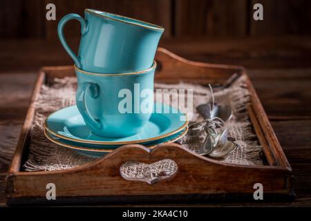 Blaue Kaffeetassen und Löffel auf altem Holztablett Stockfoto