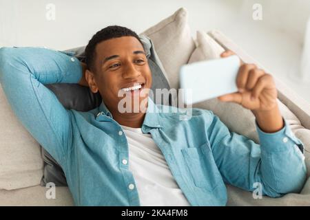 Happy Millennial african american guy haben Videoanruf, beobachten lustige Videos auf dem Smartphone in der Freizeit Stockfoto