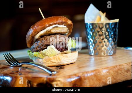 Großer Hamburger mit karamellisierten roten Zwiebeln und frittierten französischen Speisen auf Holzschneidebrett Stockfoto