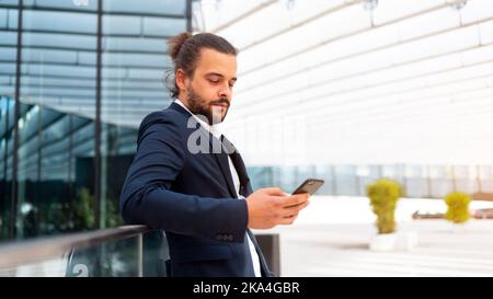 Geschäftsmann im Freien stehend verwenden Smartphone suchen Gerät Bildschirm zuversichtlich. Gutaussehender hispanischer männlicher Geschäftsmann im mittleren Alter gekleidet Geschäftsanzug mit Smartphone in der Hand. Moderne Geschäftsleute Stockfoto