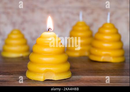 Bienenwachskerzen in Form von Skeps auf Holzhintergrund, Kerze von vorne angezündet Stockfoto