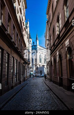 Eine vertikale Aufnahme einer Gasse mit einer Kirche am Ende einer alten europäischen Kopfsteinpflasterstraße in Riga, Lettland Stockfoto