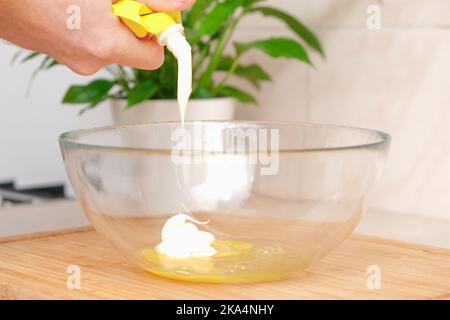 Transparente Glasschüssel mit Hühnereichen. Der Prozess der Herstellung der Sauce. Der Prozess der Zugabe von Mayonnaise zu einer transparenten Glasschüssel mit einem Hühnereier. Der Prozess des Kochens zu Hause. Stockfoto