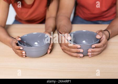 Hände eines jungen schwarzen Paares mit leeren Tellern auf einem Holztisch, die unter Hunger und Unterernährung leiden Stockfoto