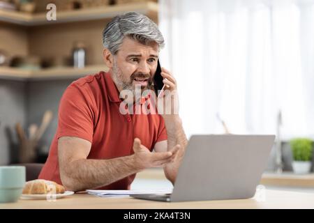 Wütender Unternehmer mittleren Alters, der von zu Hause aus arbeitet und einen Anruf hat Stockfoto