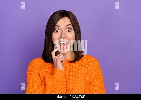 Foto-Porträt von niedlichen jungen Mädchen erstaunt Reaktion berühren Kinn gekleidet stilvolle gestrickt orange aussehen auf lila Hintergrund isoliert Stockfoto