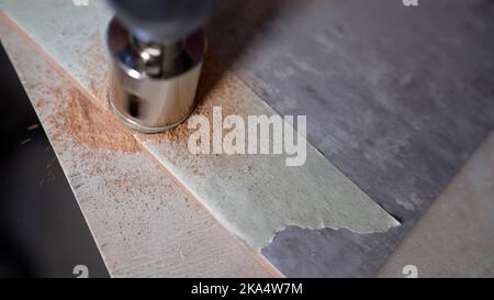 Eine Fliese verwendet eine Diamantkrone, um Löcher in die Keramikfliese zu bohren. Ein Arbeiter bohrt ein Loch in eine Keramikfliese. Stockfoto