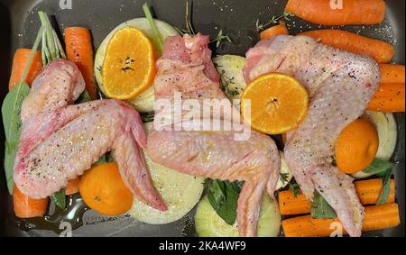 Ansicht von oben auf rohe Hähnchenflügel, Karotten, Zwiebeln, Orange, Thymian und Salbei in einer Bratpfanne, um eine Soße zu machen Stockfoto