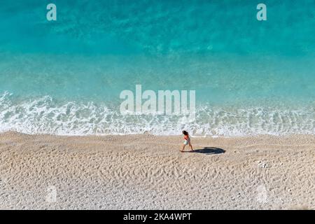 Ein Tourist, der an einem schönen Sandstrand mit sanften Wellen und kristallklarem Wasser spazieren geht. Stockfoto