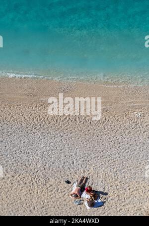 Ein wunderschöner Sandstrand mit kristallklarem Wasser und einem Paar, das seinen Urlaub genießt. Stockfoto