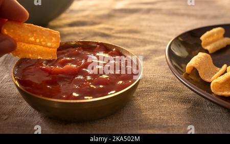 Eine Hand, die einen Kartoffelchip in eine Salsa taucht Stockfoto