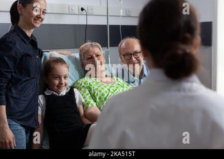 Ärztin besucht ältere Frau, die sich im Sanatoriumbett ausruht. Krankenschwester überprüft den Fortschritt der alten Patientenwiederherstellung. Ältere Dame mit Atemproblemen, die dem Geriatrie die Symptome erklärt. Stockfoto