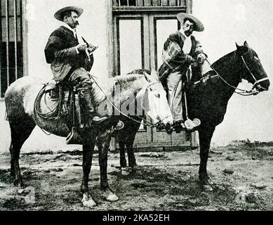 Diese Abbildung aus dem Jahr 1914 zeigt zwei Reiter (oder Cowboys) in Chile. Der Bildunterschrift zufolge wird ein chilenischer Cowboy oder Reiter nie ohne seinen breiten Rundkrempelhut, seinen bunten Umhang und seinen Bandschlitz um die Taille gesehen. Sie sind als Guasos oder huasos bekannt. Stockfoto