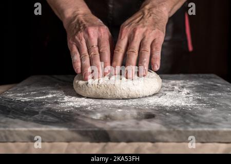 Mann bereitet Pizza, Teig auf Marmortisch zu. Stockfoto