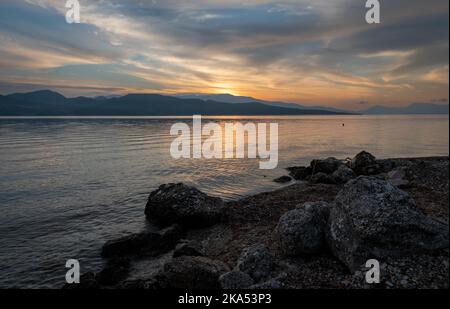 Die Sonne, die über dem Hügel aufgeht, wirft goldene Lichtreflexe auf das ruhige Meer. Stockfoto