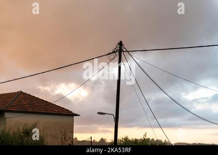 Eine Stromleitung auf einem Holzpfahl über dem Kopf, die Strom zu einem Haus in einem ländlichen Gebiet liefert. Stockfoto