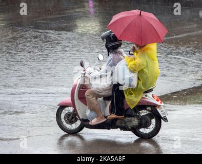 Ein Paar mit einem Regenschirm fährt im Regen ein Motorrad Stockfoto