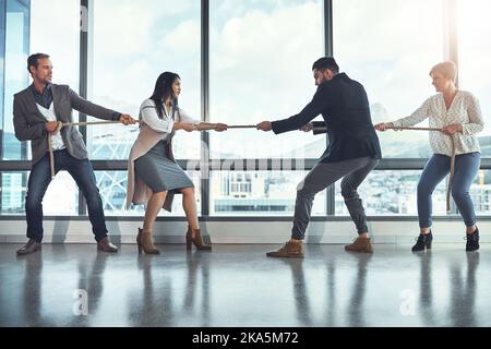 Die Geschäftswelt ist ziemlich konkurrenzfähig. Eine Gruppe von Geschäftsleuten, die während des Tauschens in einem Büro an einem Seil ziehen. Stockfoto