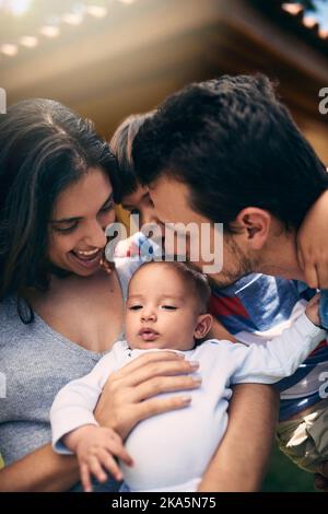 Sie können nicht genug von ihrem neuesten Zusatz erhalten. Eine liebevolle junge Familie, die Zeit mit ihrem Baby verbringt, während sie in ihrem Hinterhof zu Hause steht. Stockfoto