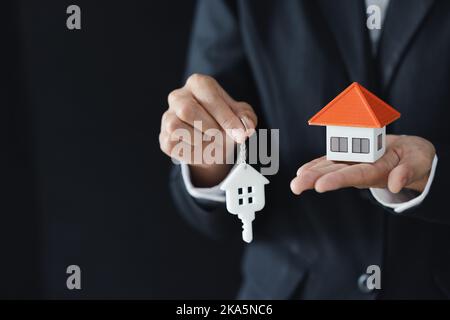 Hausmodelle und Münzen in menschlichen Händen, Hypothekenkonzept von Geldhaus aus den Münzen. Stockfoto