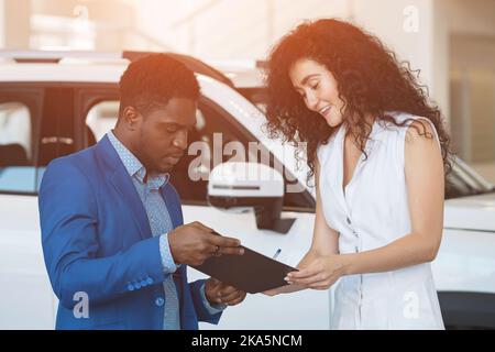Der Kunde wählt ein Auto und unterzeichnet im Salon einen Vertrag über den Verkauf von Autos Stockfoto