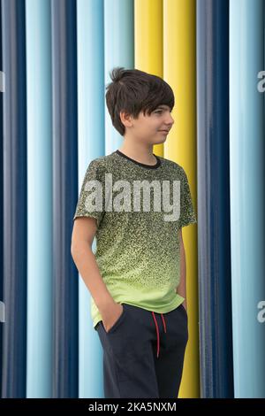 Kaukasischer Junge in Sportkleidung, mit Händen in den Taschen, lächelnd und auf farbenfrohem Hintergrund blickend Stockfoto