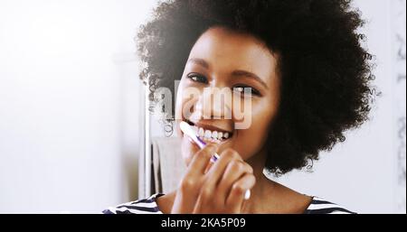 Routinen am frühen Morgen. Porträt einer fröhlichen jungen Frau, die sich die Zähne putzt, während sie ihre Spiegelung im Spiegel im Badezimmer zu Hause betrachtet. Stockfoto