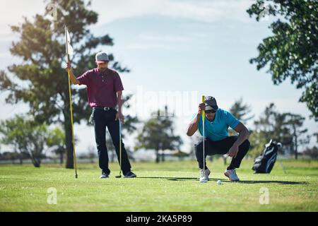 Erste Runden auf mich, wenn dies geht in. Ein fokussierter junger männlicher Golfspieler Blick auf einen Golfball, während er auf dem Gras draußen während des Tages sitzen. Stockfoto