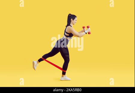 Die Sportlerin arbeitet mit Gummiband und Hanteln auf lebhaft gelbem Hintergrund. Stockfoto