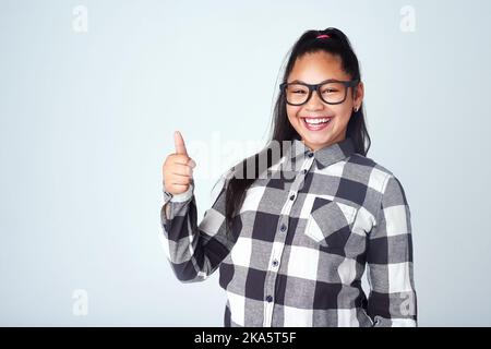 Hey, gute Arbeit. Studio-Portrait eines niedlichen jungen Mädchens, das vor grauem Hintergrund Daumen hoch gibt. Stockfoto