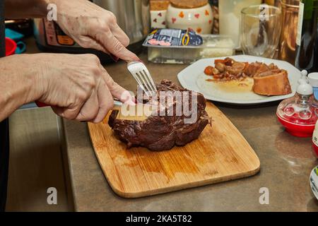 Der Koch schneidet Scheiben aus einem Stück lang gegartem Rindfleisch Stockfoto